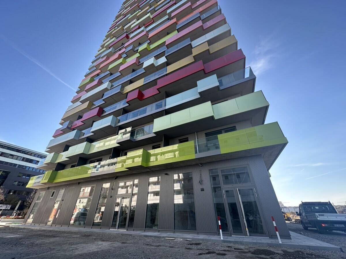 Hohes, modernes Gebäude mit farbenfrohen Balkonen und großen Glasflächen unter blauem Himmel.