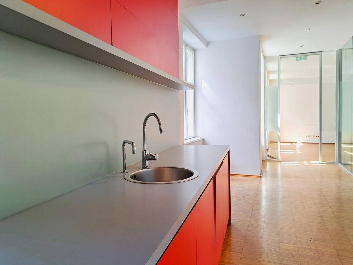 Moderne Teeküche mit roter Schrankfront, Spülbecken und Blick in den angrenzenden Bürobereich.