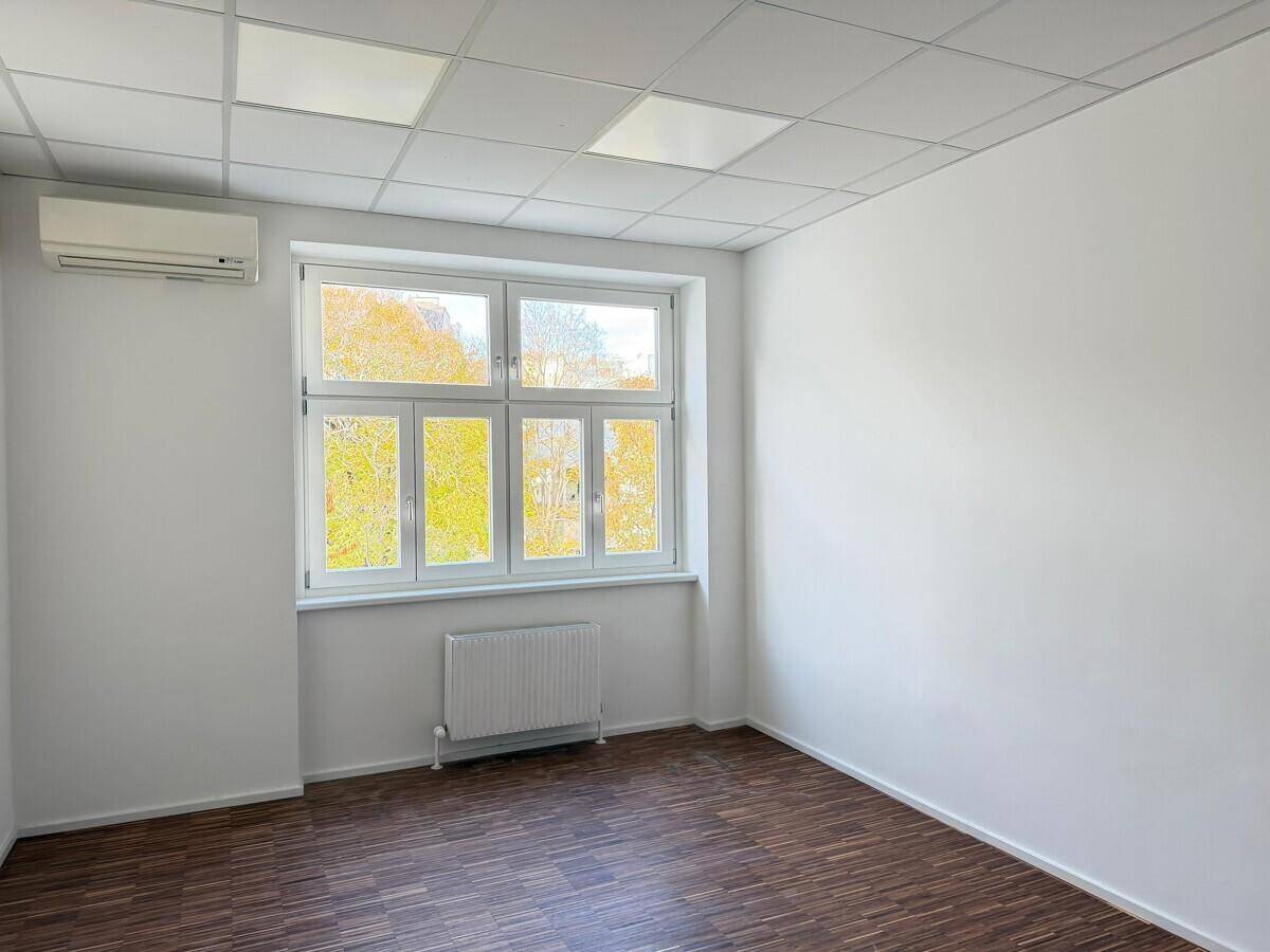 Heller Büroraum mit Klimaanlage, großen Fenstern und abgehängter Decke, ideal für konzentriertes Arbeiten.