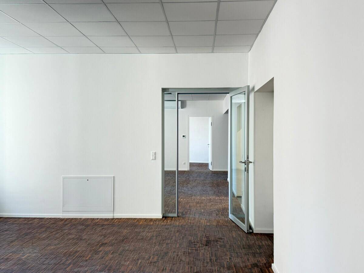Blick von einem Büroraum in einen Flur mit dunklem Holzfußboden und modernen Glastüren.