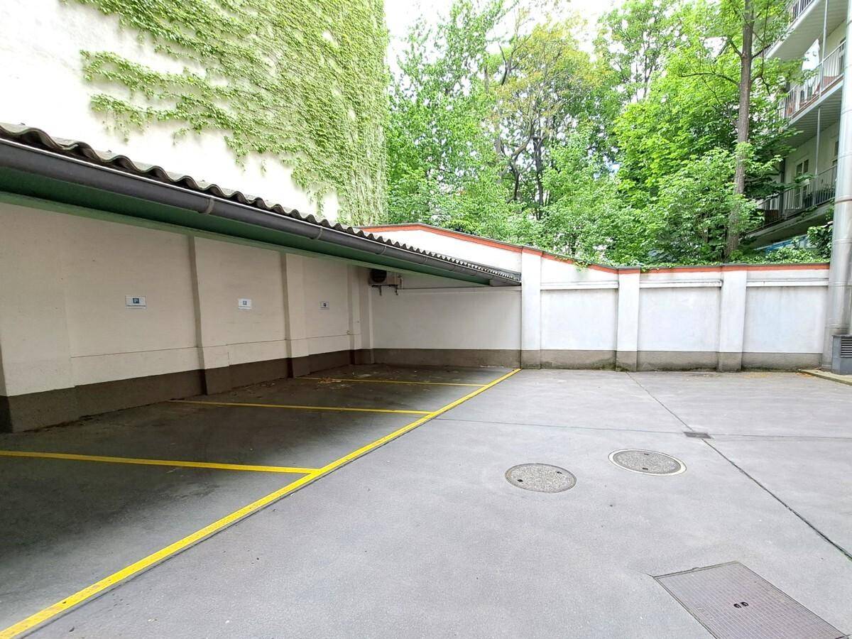 Überdachte Parkplätze im Freien mit gelben Markierungen und viel Grün im Hintergrund.