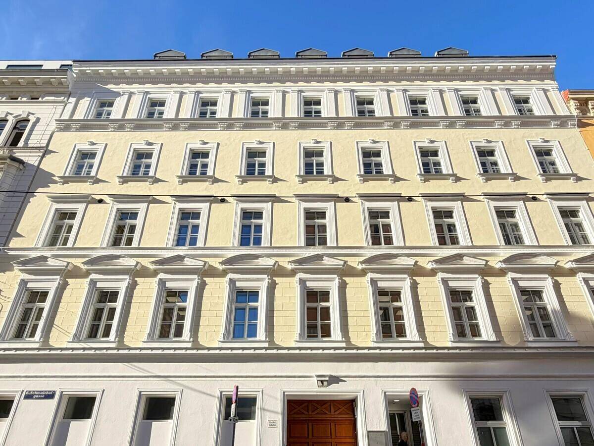 Klassische Fassade eines Altbaus mit vielen Fenstern und dekorativen Elementen unter blauem Himmel.