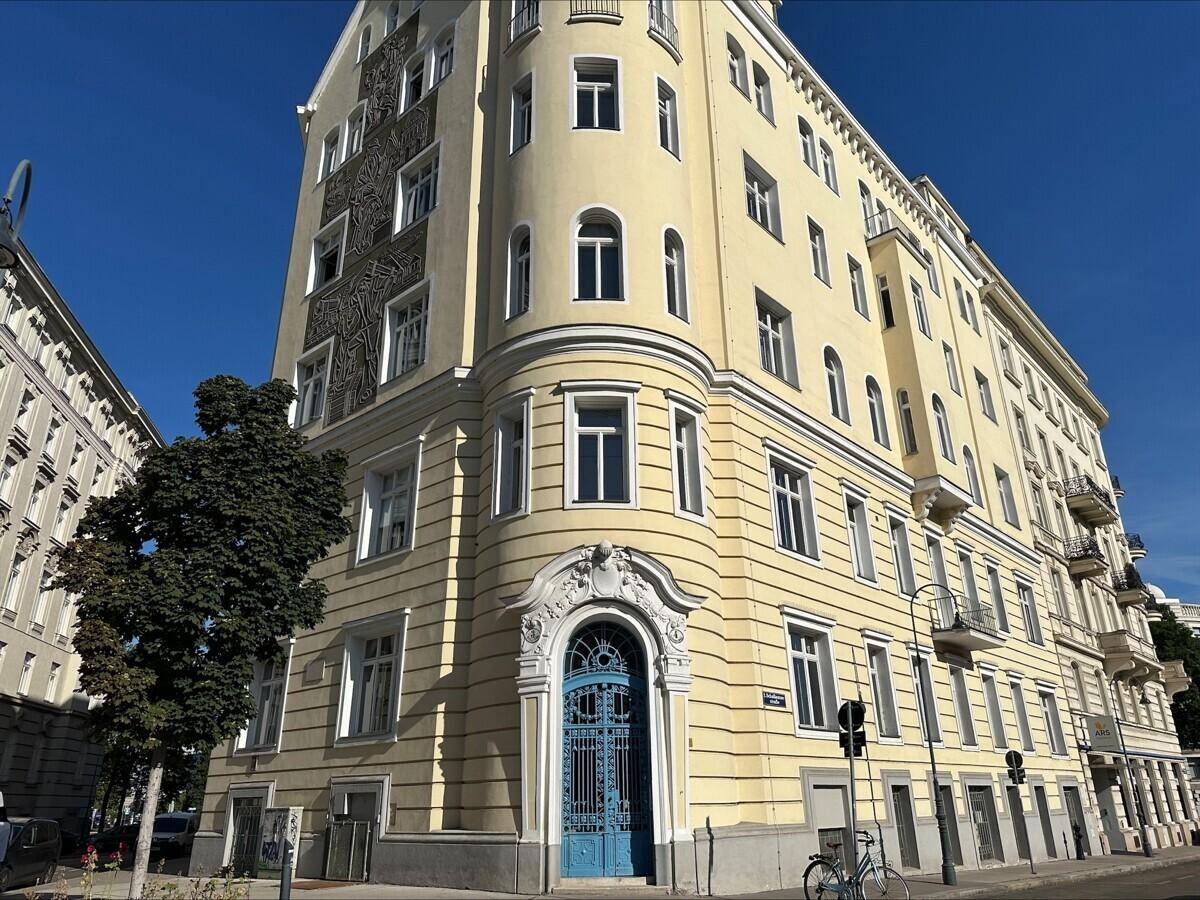 Historisches Eckgebäude mit gelber Fassade, blauer Eingangstür und dekorativen Elementen unter blauem Himmel.