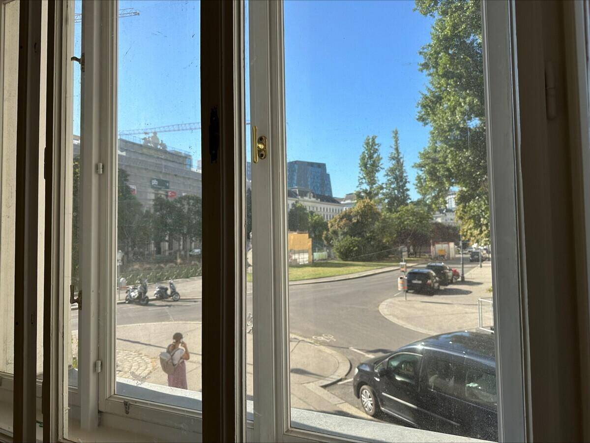 Blick aus dem Fenster eines Büros auf eine belebte Straße mit Bäumen und Gebäuden im Hintergrund.