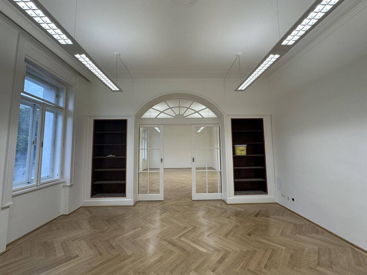 Großes Büro mit Fischgrätparkett, Einbauregalen und einer eleganten Doppeltür zu einem weiteren Raum.