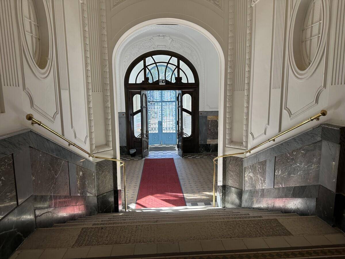 Repräsentativer Eingangsbereich mit breiter Treppe, Marmorverkleidung und einem roten Teppich zum Hauptportal.