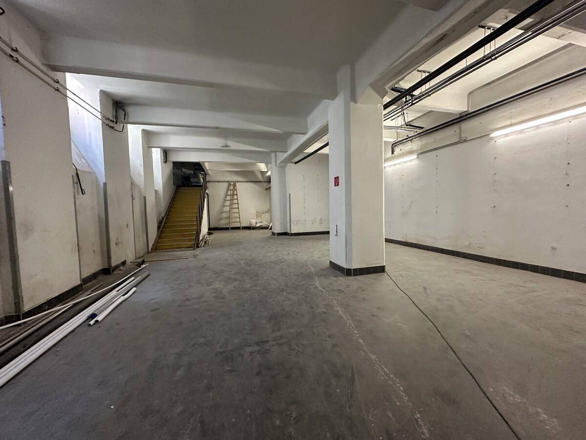 Geräumiger Kellerbereich mit Betonboden, Säulen und einer Holztreppe, die nach oben führt.