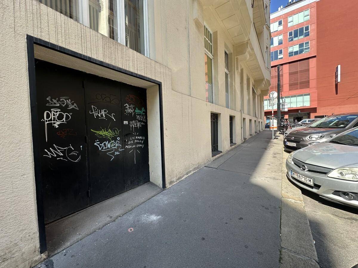 Seitlicher Eingang mit schwarzen Türen, die mit Graffiti versehen sind, an der Gebäudeseite.