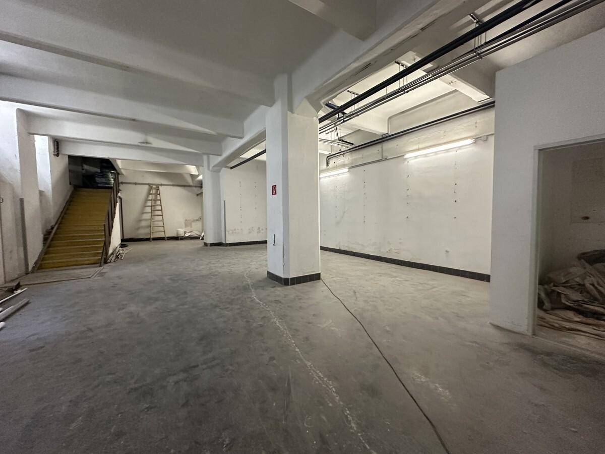 Großer Kellerraum mit tragenden Säulen und einer Treppe, die in ein höheres Stockwerk führt.