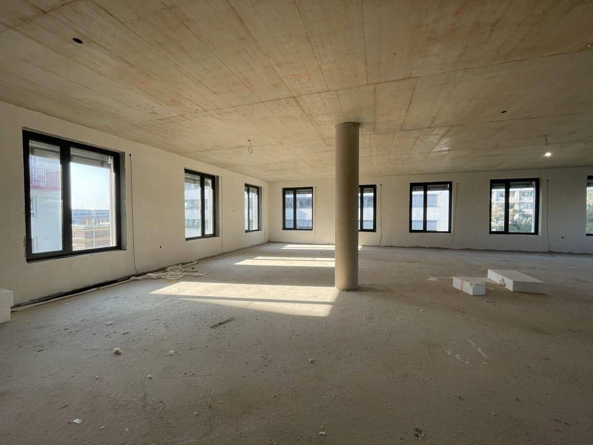 Großer, unfertiger Büroraum mit Betonboden und -decke, vielen Fenstern und einer Säule.