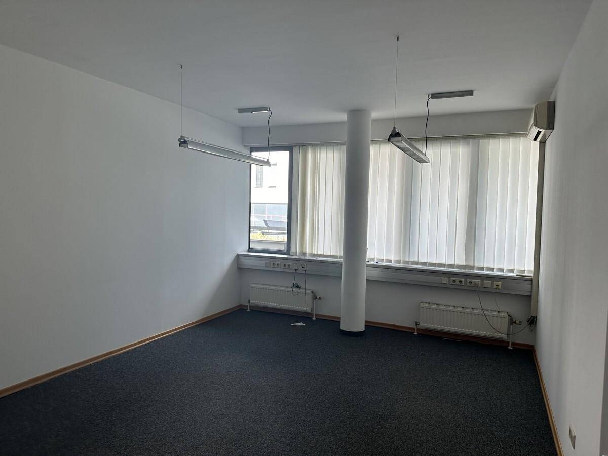 Helles Büro mit Teppichboden, Säule, großen Fenstern mit Jalousien und Klimaanlage.