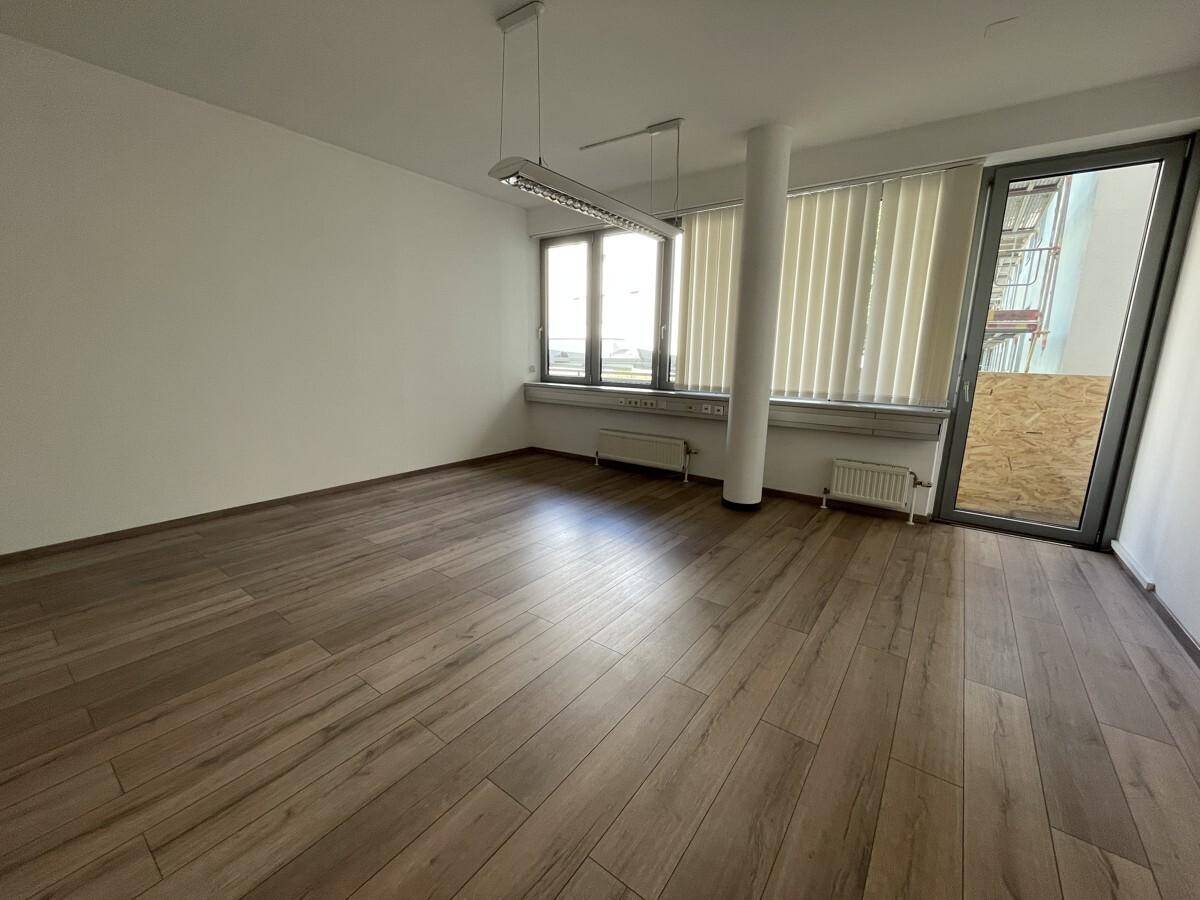 Leerer Raum mit Laminatboden in Holzoptik, großen Fenstern, Heizkörpern und Zugang zu einem Außenbereich.