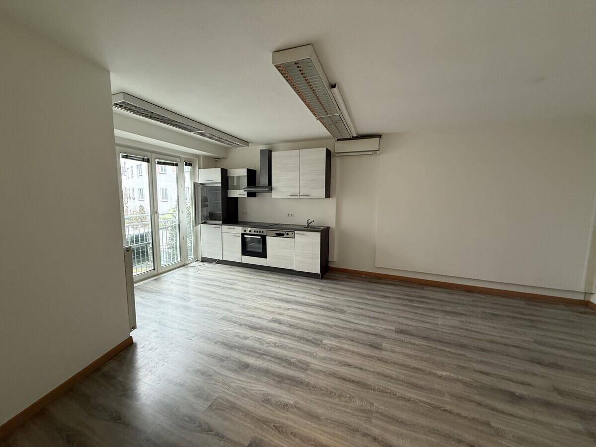 Heller Raum mit integrierter Küchenzeile, Laminatboden und Zugang zu einem Balkon.