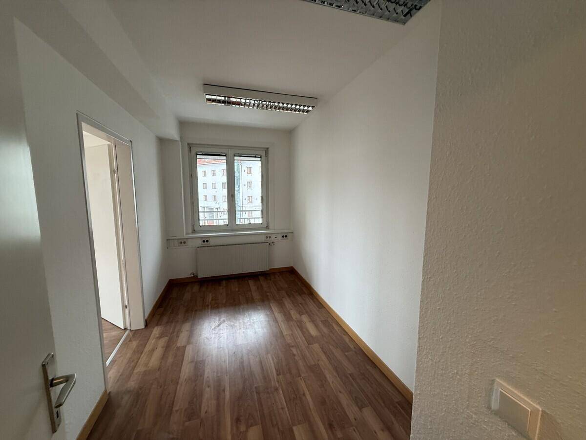 Kleinerer Büroraum mit einem Fenster, Laminatboden und weiß gestrichenen Wänden, bereit zur Einrichtung.