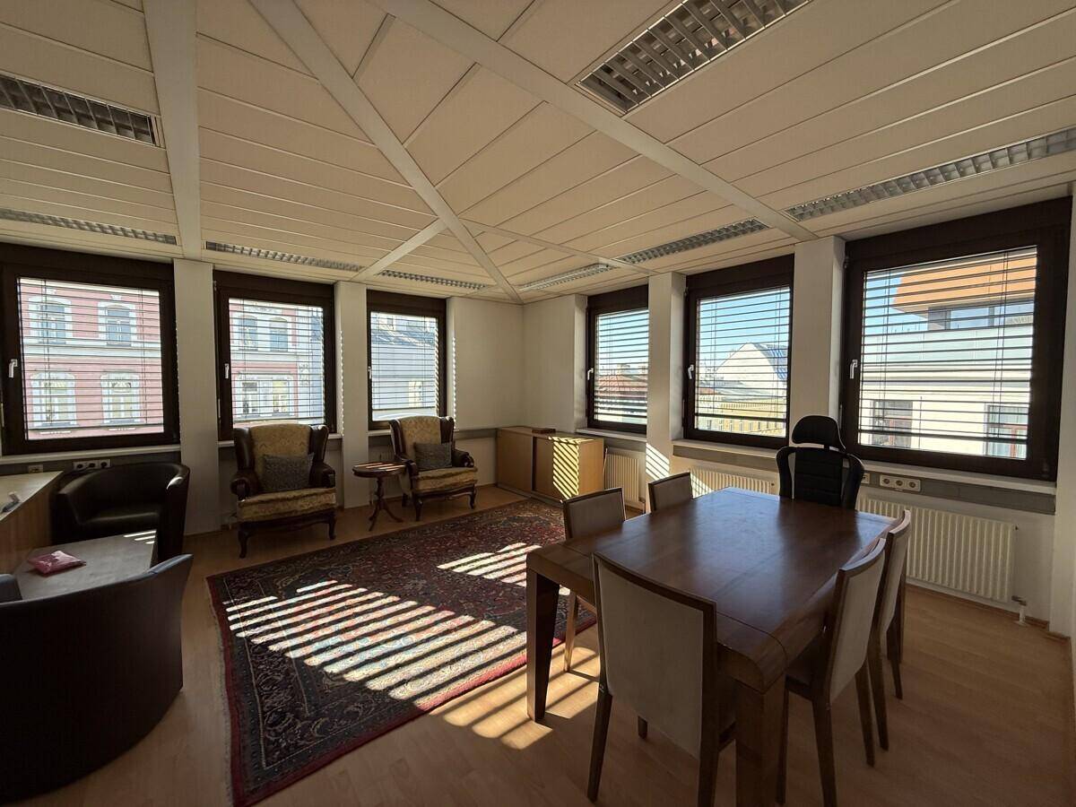 Helles und geräumiges Büro mit einem großen Holztisch, Schreibtischen und vielen Fenstern.
