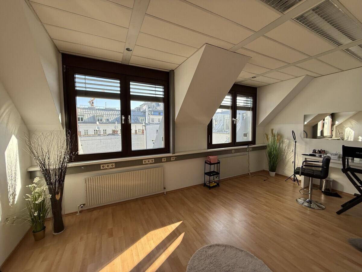 Geräumiger Büroraum mit Dachschrägen, großen Fenstern und Holzboden, hell beleuchtet durch Sonnenlicht.