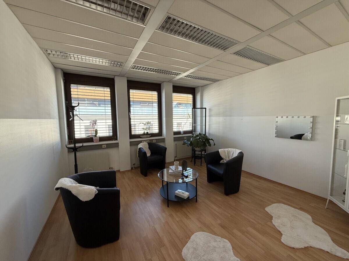 Geräumiger Büroraum mit drei schwarzen Sesseln, einem Couchtisch und großen Fenstern, gut beleuchtet.