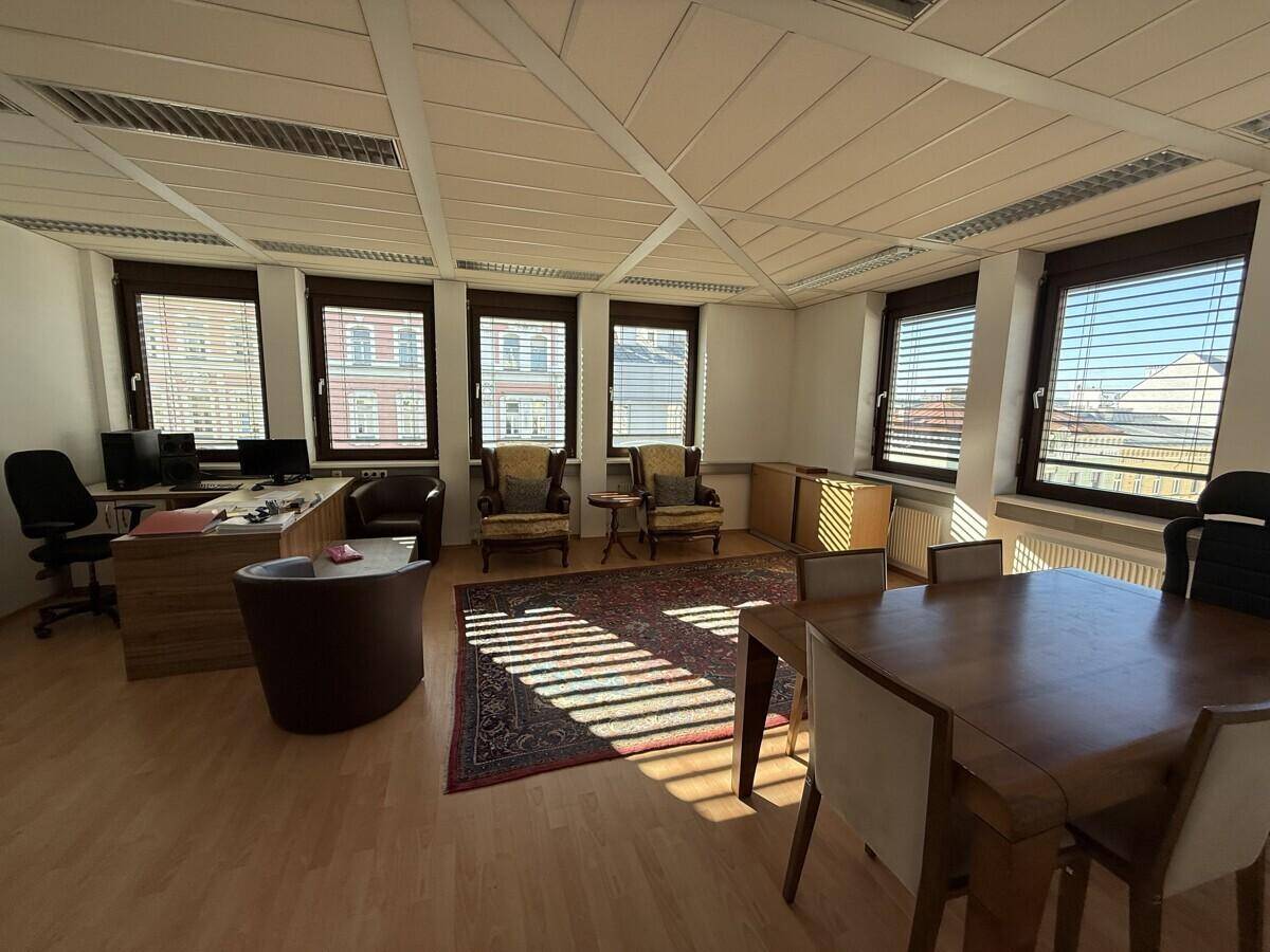 Großes Büro mit mehreren Arbeitsbereichen, einem Konferenztisch und vielen Fenstern mit Jalousien.