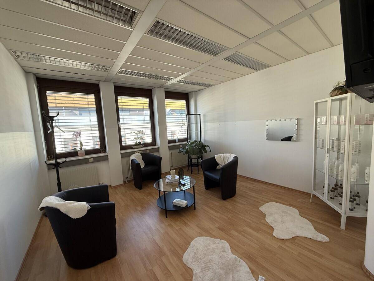 Heller Büroraum mit drei schwarzen Sesseln, einem runden Couchtisch und großen Fenstern.