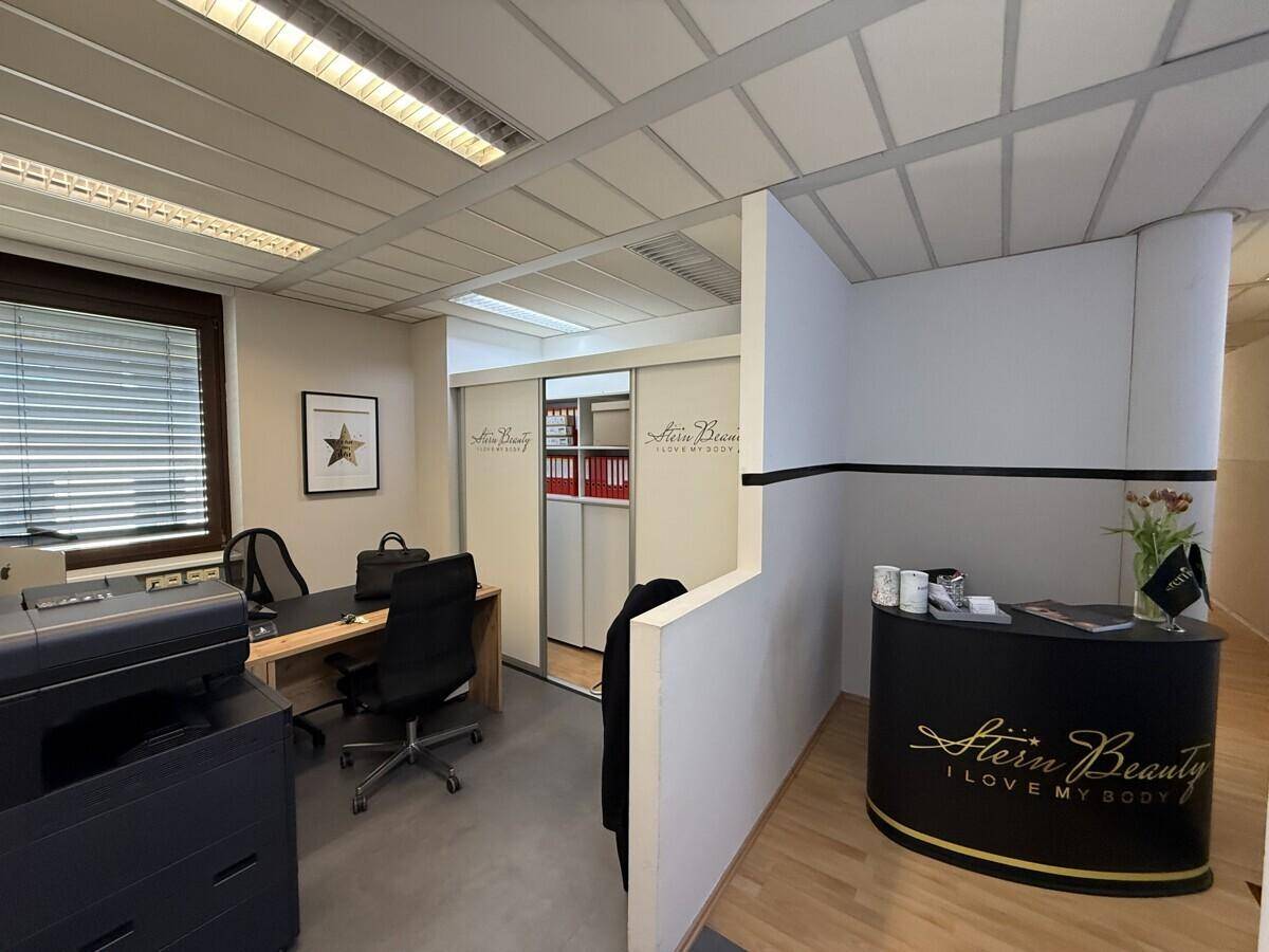 Modernes Büro mit Empfangsbereich, Schreibtisch und Stauraum, gut beleuchtet durch Fenster.