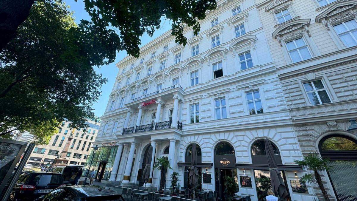 Eindrucksvolles, klassisches Gebäude mit weißer Fassade und Geschäften im Erdgeschoss an einer belebten Straße.