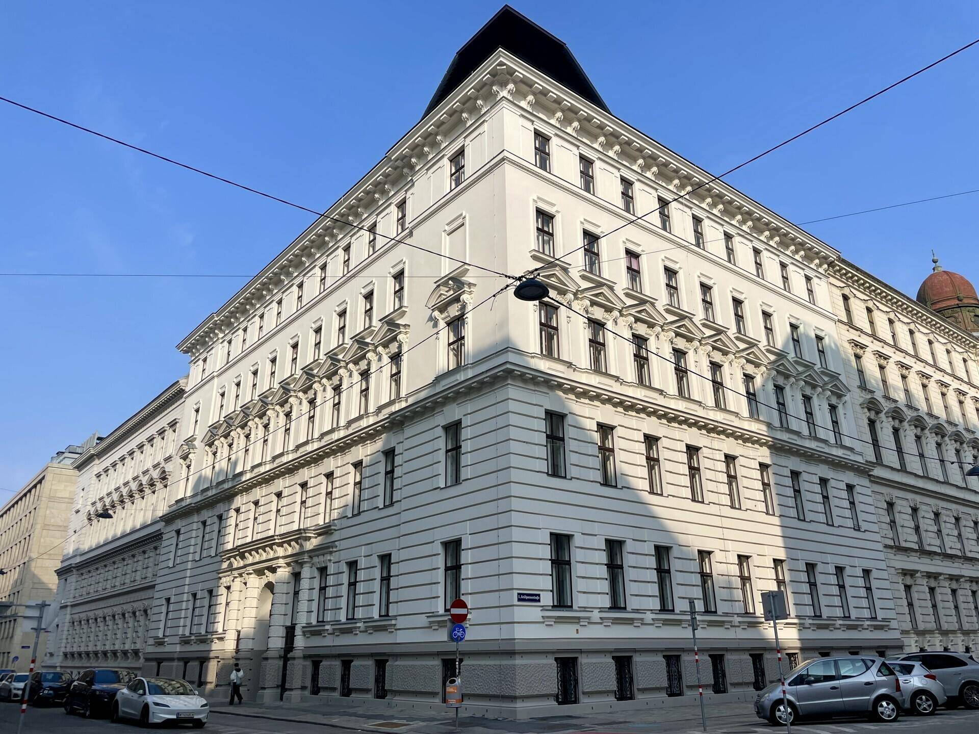 Weitwinkelansicht des historischen Eckgebäudes an einer belebten Straße unter blauem Himmel.