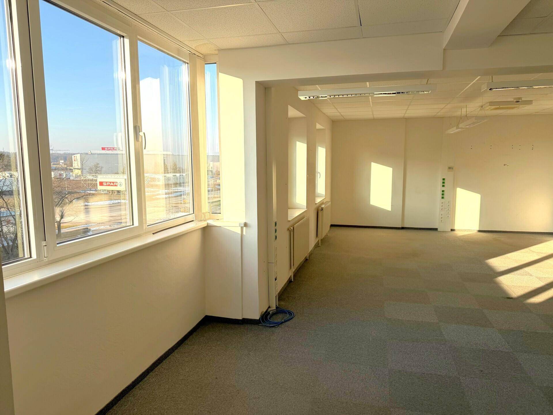 Helles Büro mit großen Fenstern, Teppichboden und Blick auf die Umgebung.