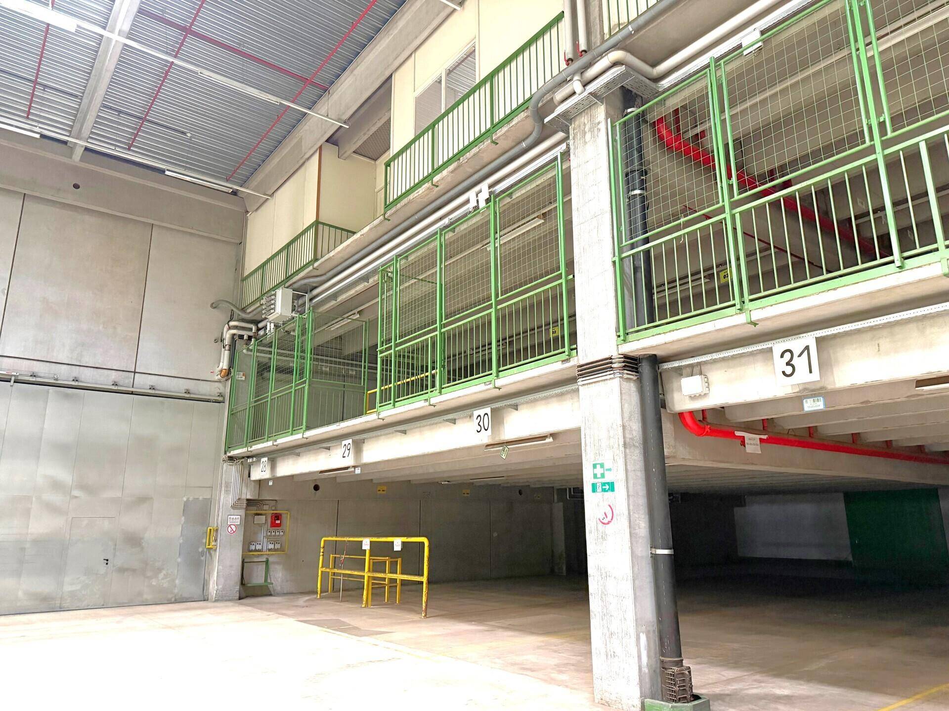 Mehrstöckiger Industriebereich mit grünen Geländern, Betonpfeilern und sichtbaren Installationen.