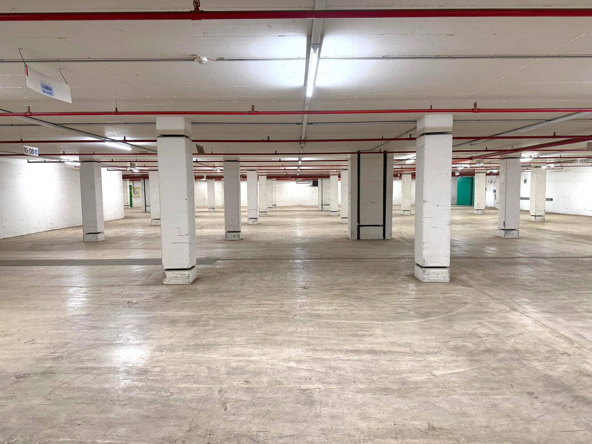 Geräumige Tiefgarage mit vielen Säulen, Betonboden und sichtbaren roten Rohren an der Decke.