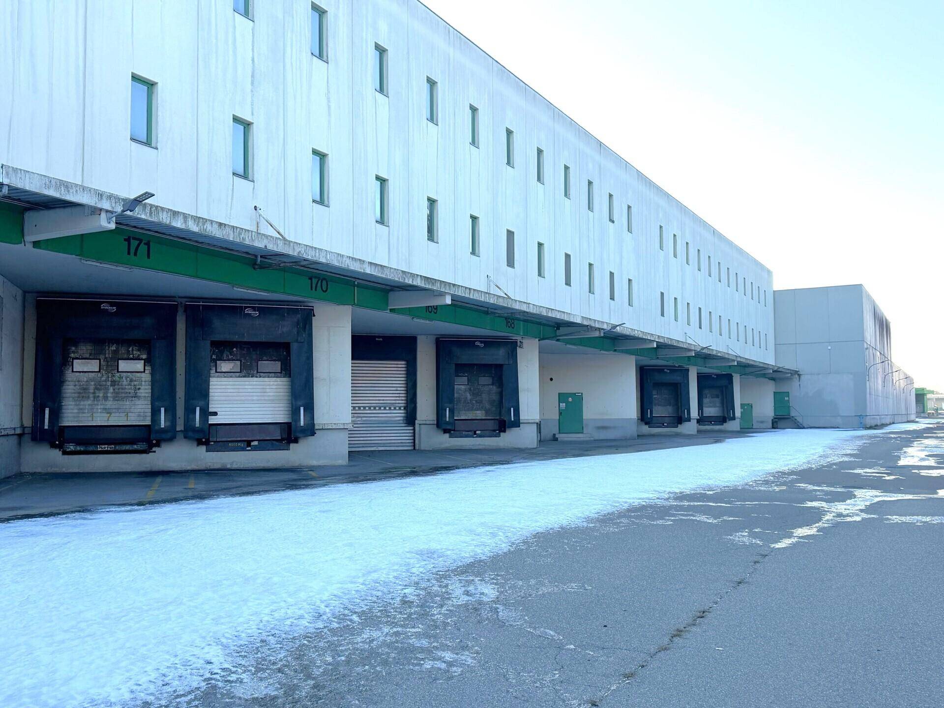 Lange Fassade eines Industriegebäudes mit zahlreichen Laderampen und etwas Schnee auf dem Vorplatz.