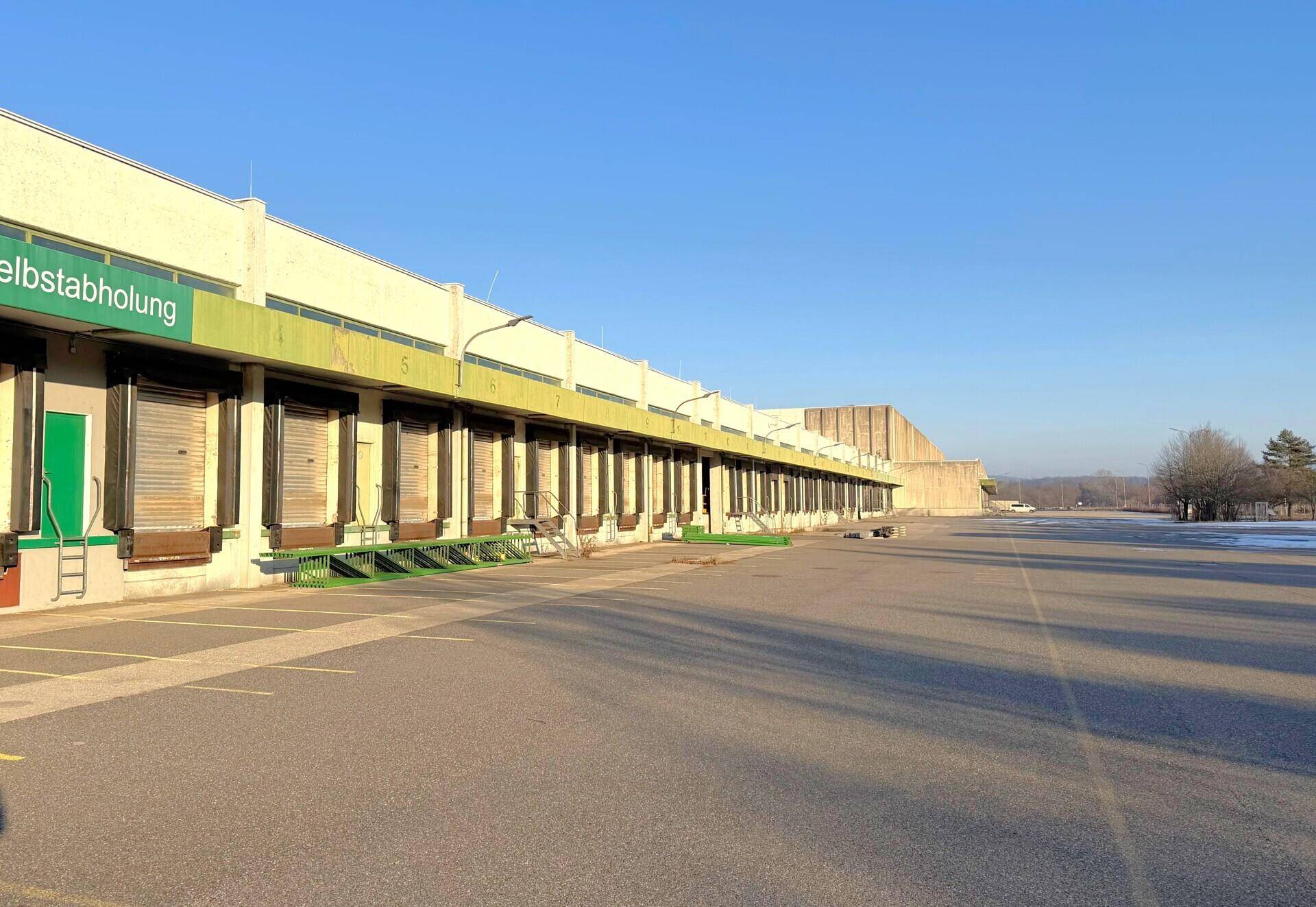 Weitläufiger Parkplatz vor einer langen Reihe von Laderampen eines großen Lagerkomplexes.