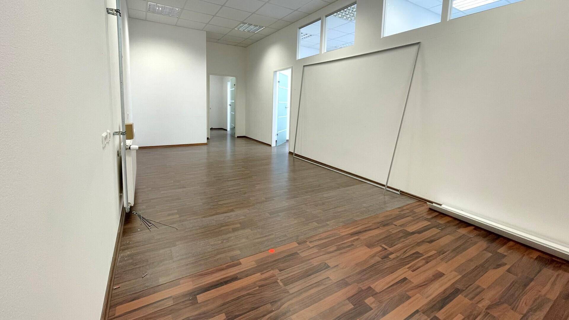 Großer, leerer Büroraum mit Holzboden, weißen Wänden und Blick in einen weiteren Flur.