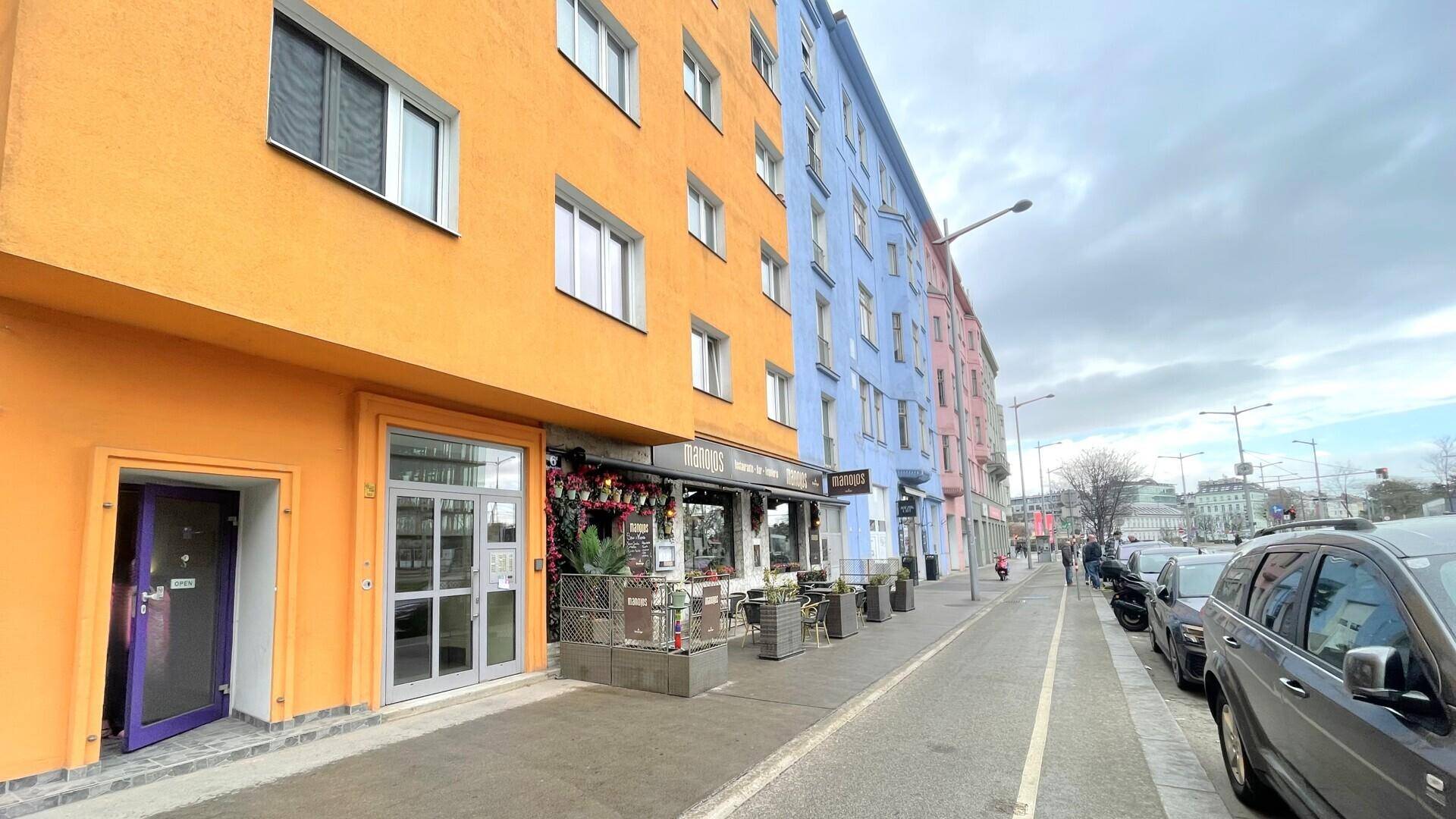 Lebhafte Straße mit farbenfrohen Gebäuden, einem Restaurant und parkenden Autos entlang des Bürgersteigs.