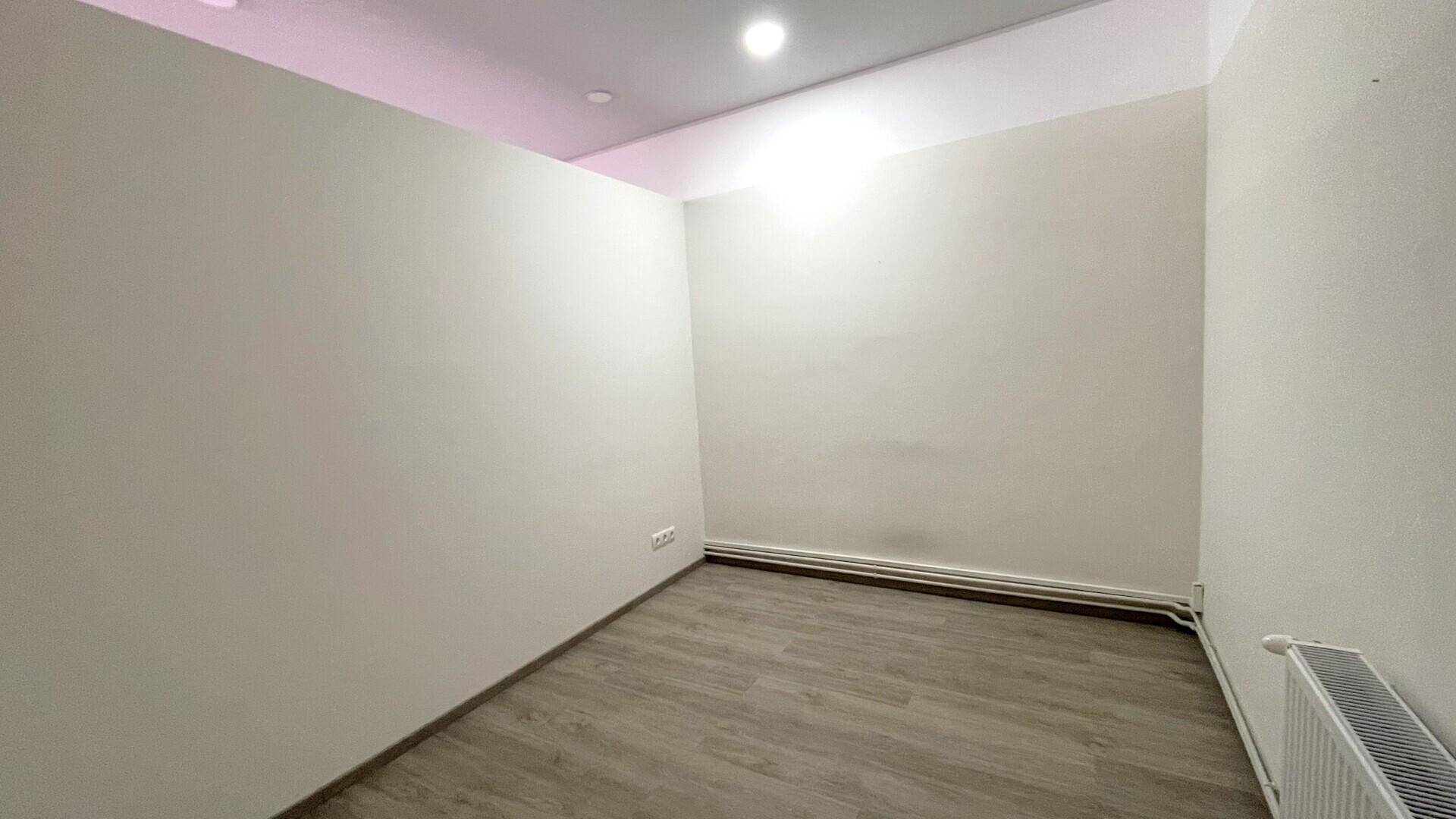 Heller Büroraum mit weißen Wänden, Holzboden und einem Heizkörper, der vielseitig nutzbar ist.