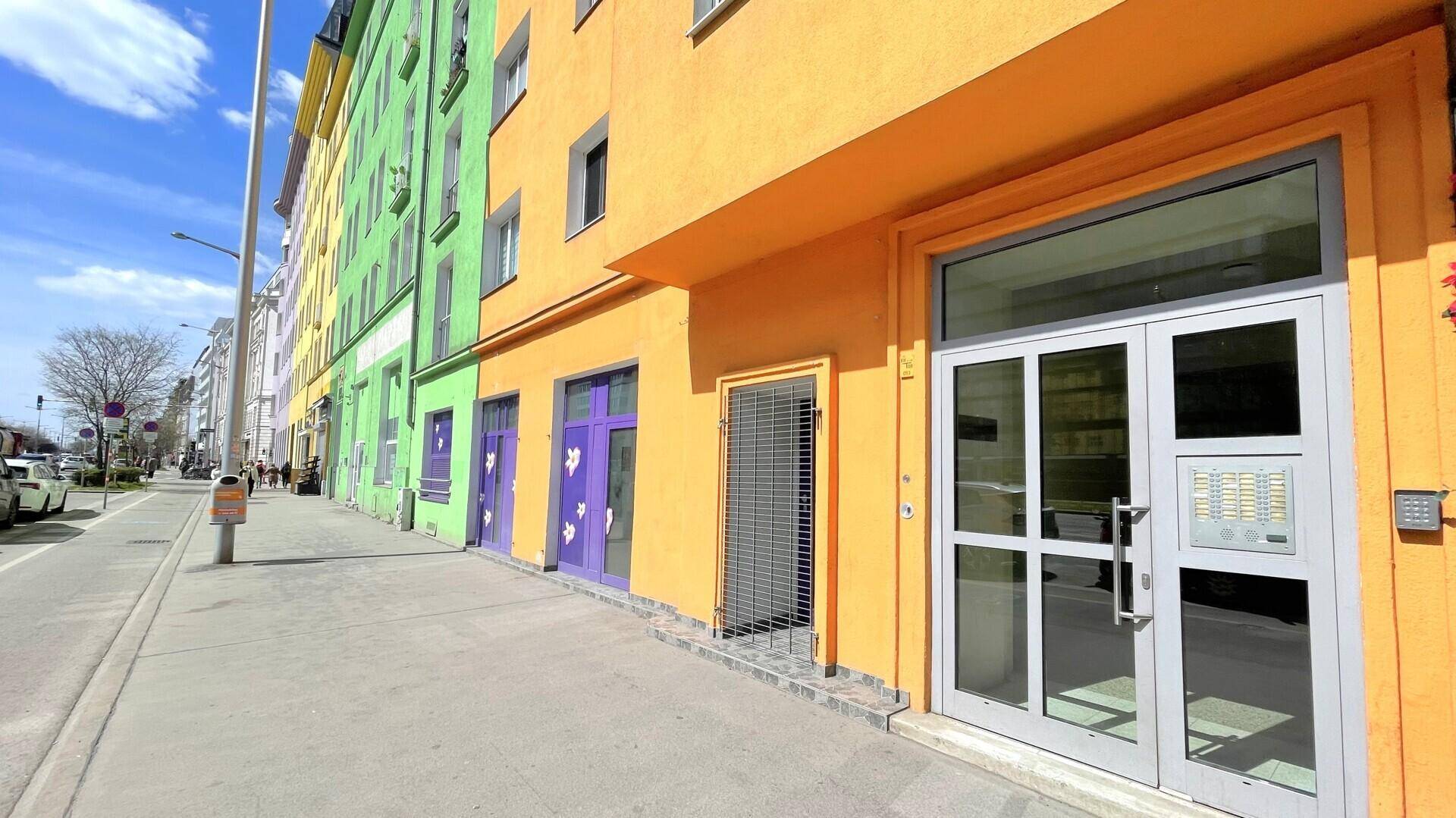 Bunte Gebäudefassade mit Geschäften im Erdgeschoss und einem breiten Bürgersteig davor.