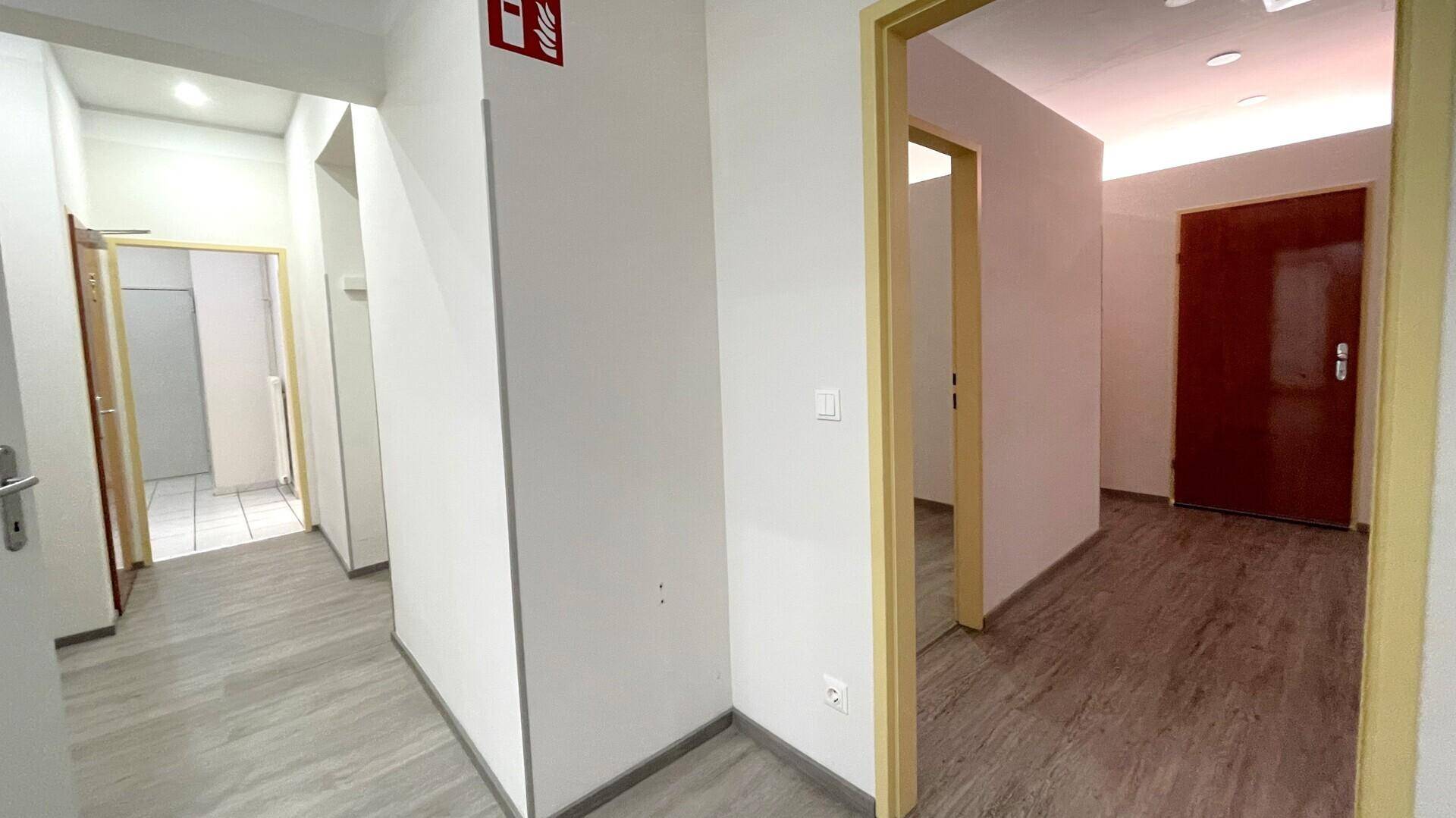 Heller Flur mit mehreren Türen und einem Feuerlöscher an der Wand, der zu weiteren Räumen führt.