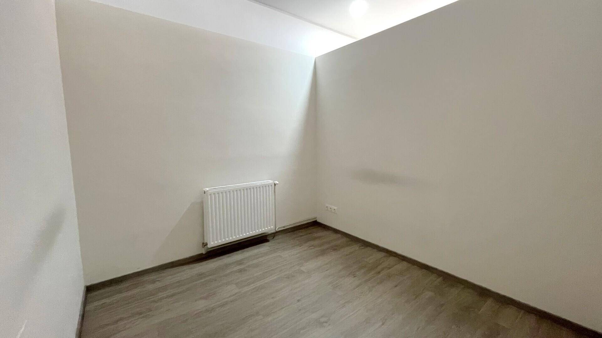 Schlichter, heller Büroraum mit weißen Wänden, Holzboden und einem Heizkörper an der Wand.