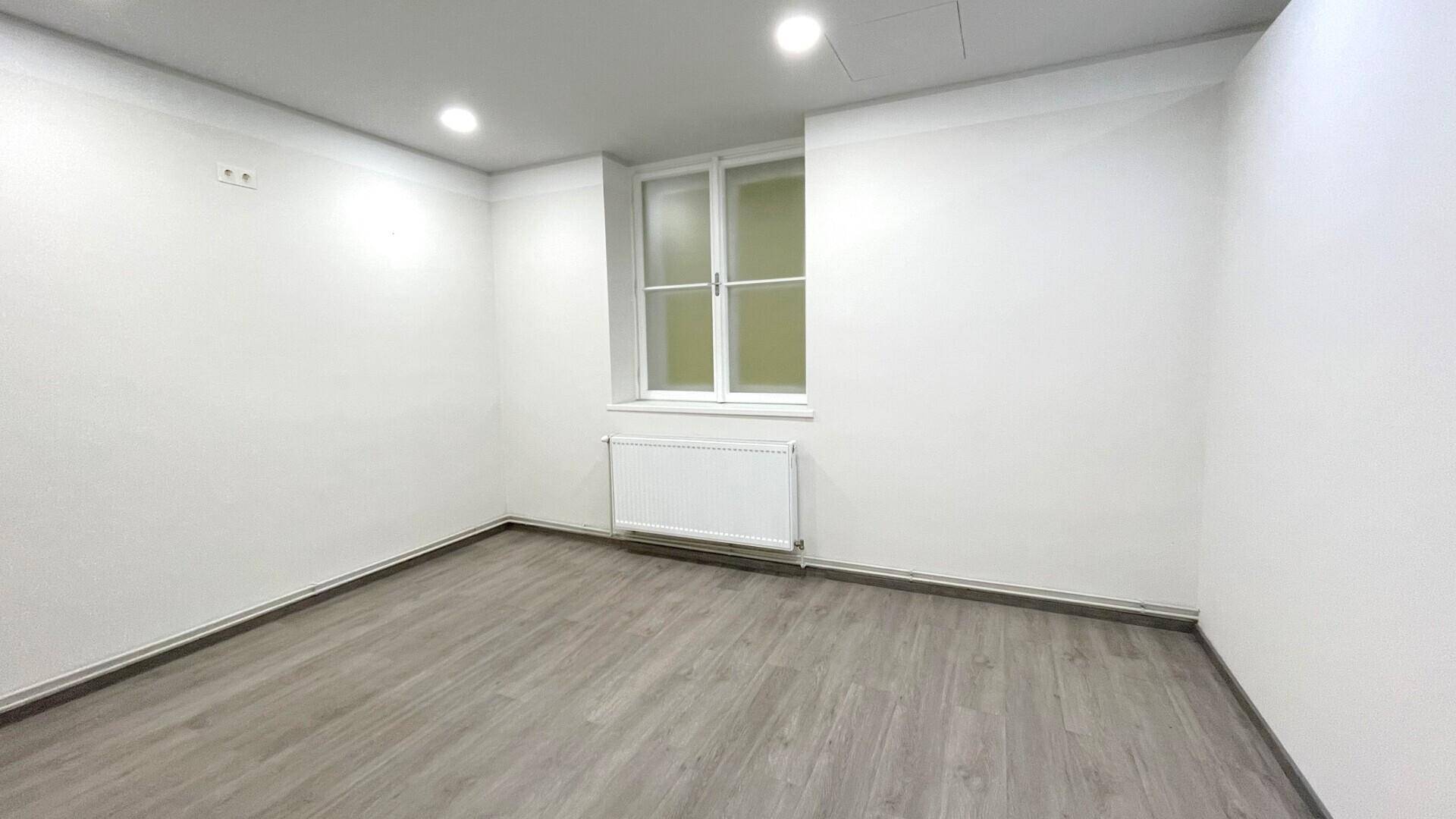 Geräumiger Büroraum mit einem Fenster, weiß gestrichenen Wänden und einem Heizkörper unter dem Fenster.