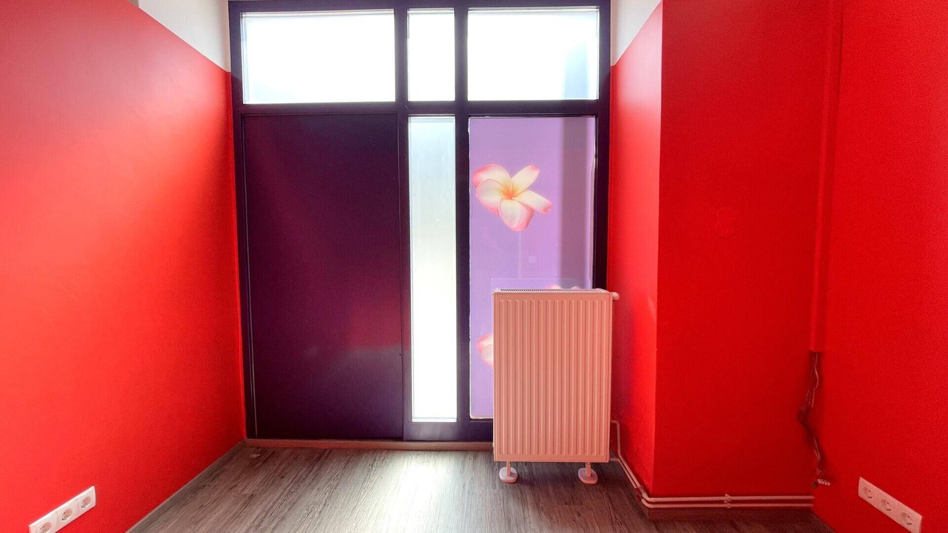Auffälliger Raum mit roten Wänden, einem großen Fenster mit Blumenmotiv und einem Heizkörper.