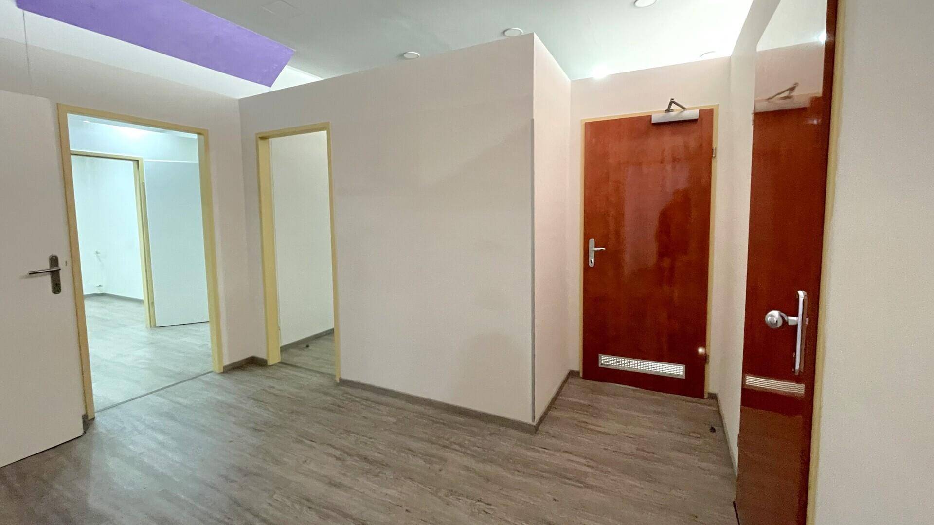 Heller Flur mit Holzboden und mehreren Türen, der zu verschiedenen Büroräumen führt.