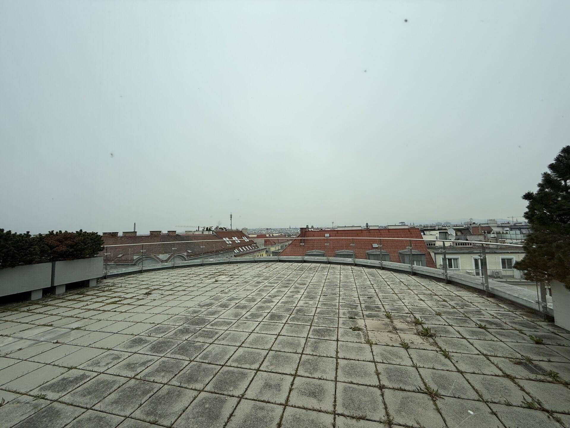 Große Dachterrasse mit Fliesenboden und weitem Blick über die Dächer der umliegenden Stadt.