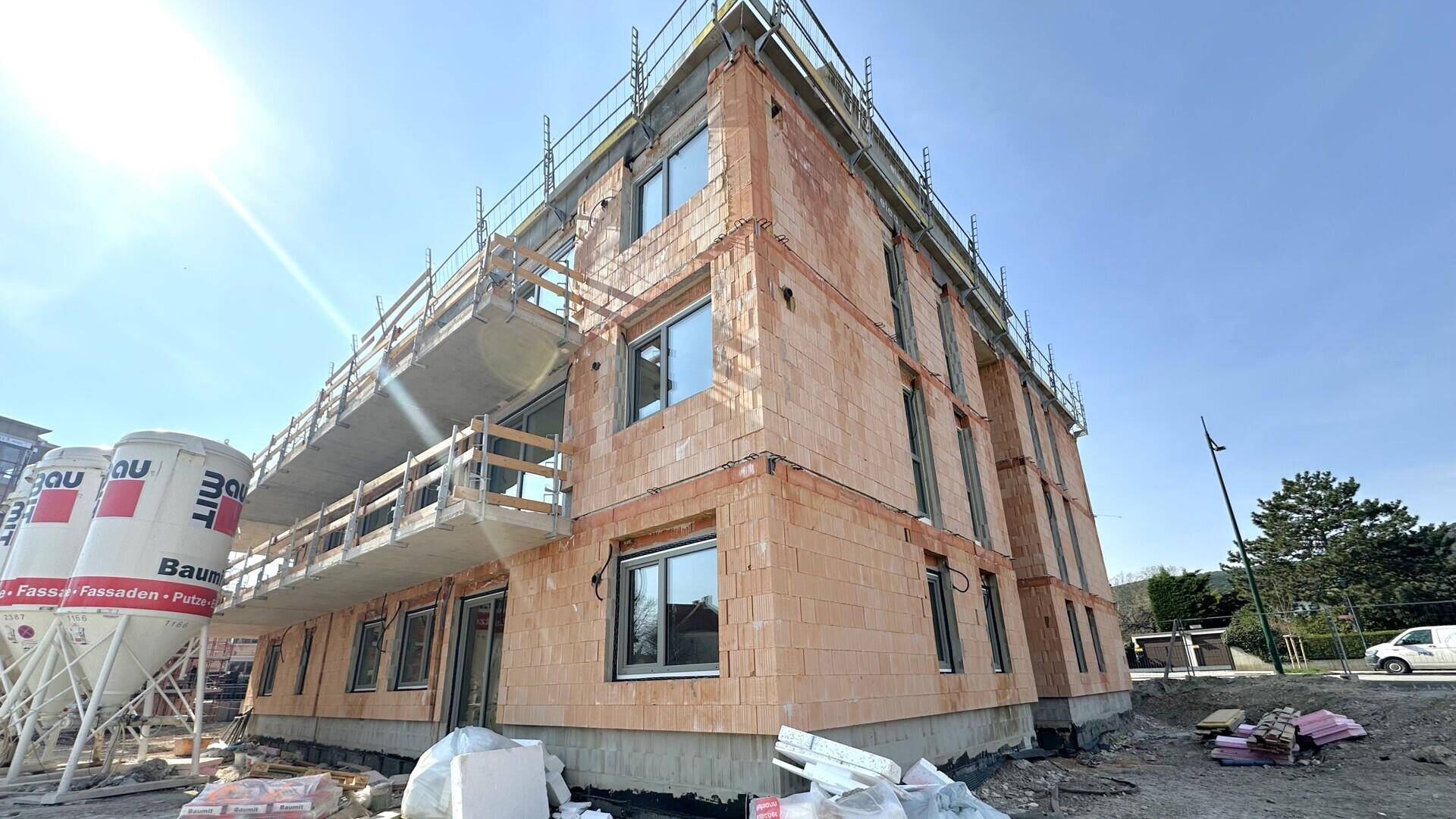 Außenansicht eines Neubaus im Rohbau mit Ziegelfassade, Gerüst und sichtbaren Baustoffen.