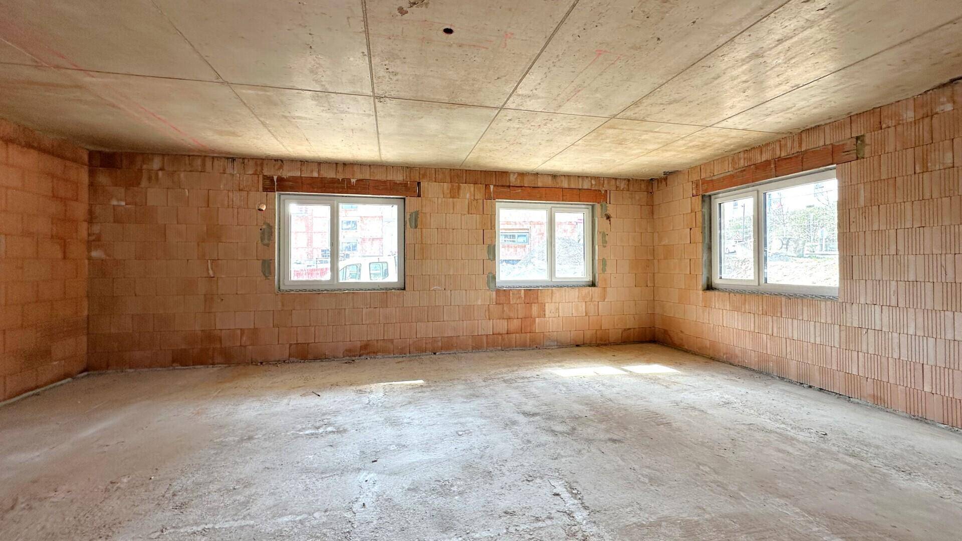 Heller Rohbau-Raum mit mehreren Fenstern und Betonboden, bereit für den Innenausbau.
