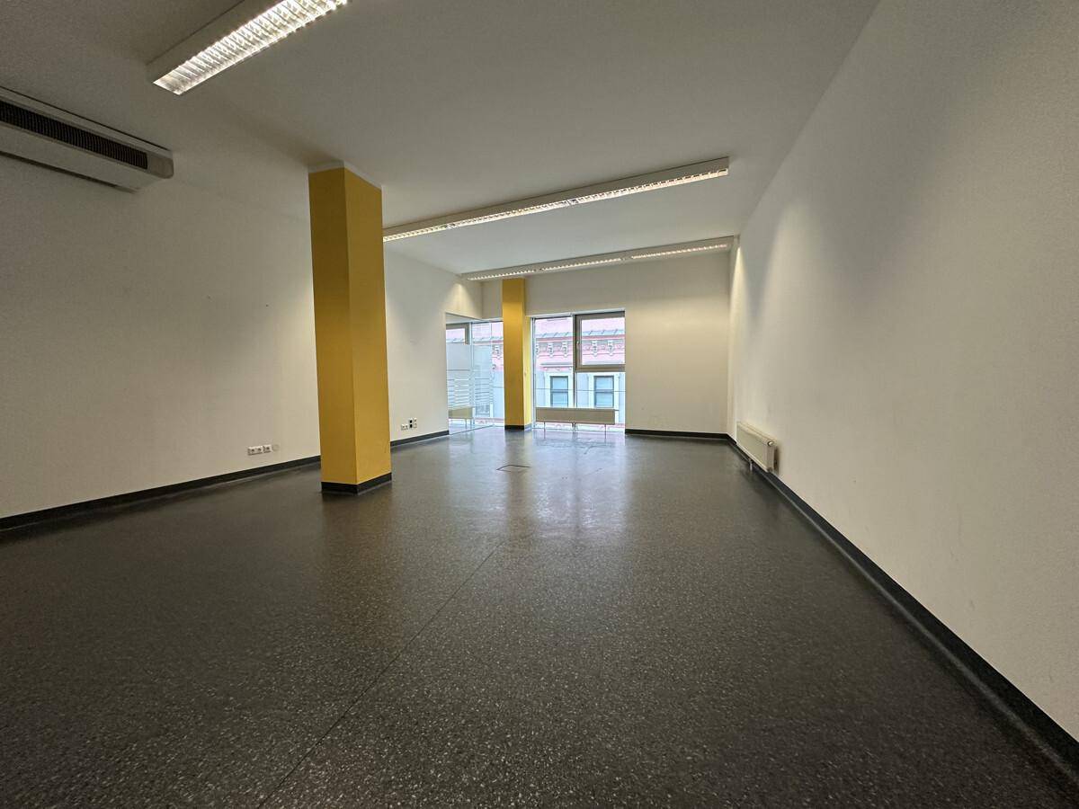 Geräumiger, leerer Büroraum mit gelbem Pfeiler, Deckenbeleuchtung und Blick durch die Fenster.