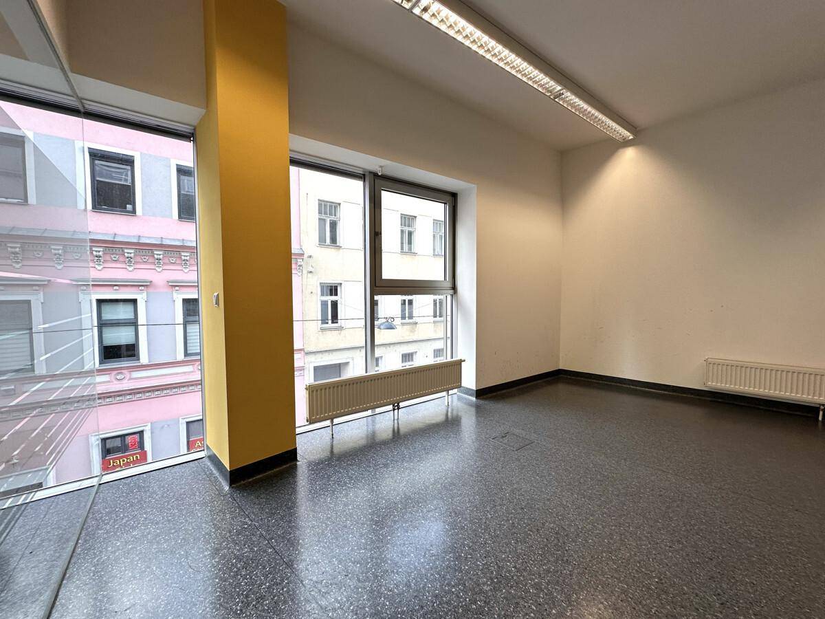Heller Büroraum mit großen Fenstern, einem gelben Pfeiler und Blick auf die umliegenden Gebäude.