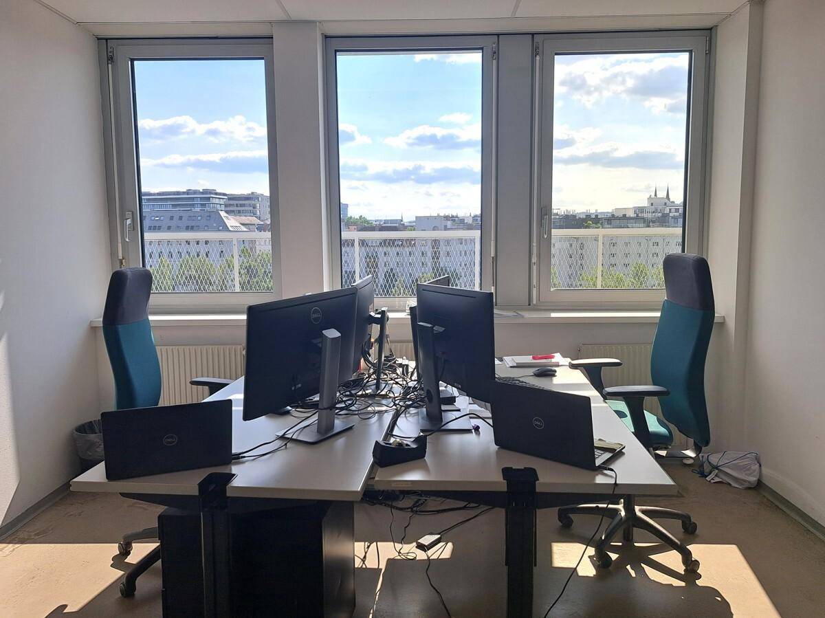Helles Büro mit mehreren Arbeitsplätzen, großen Fenstern und Blick auf die Stadtlandschaft.