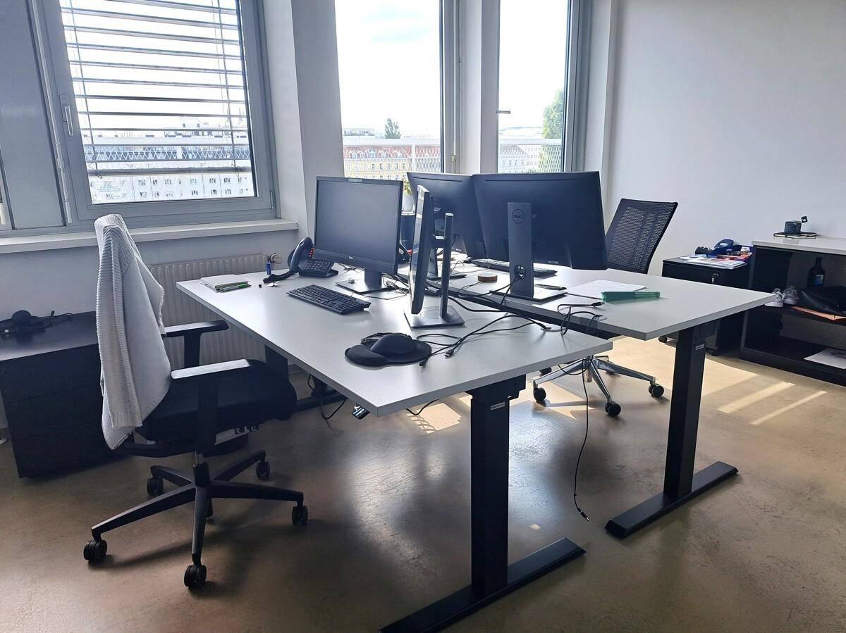 Modernes Büro mit höhenverstellbaren Schreibtischen, ergonomischen Stühlen und großen Fenstern.