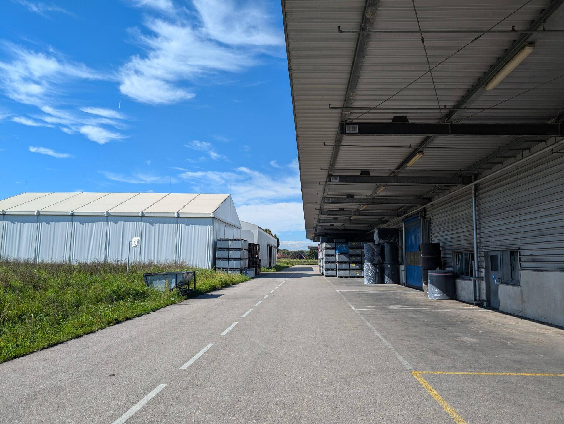 Außenbereich eines Industriegebiets mit Zufahrtsstraße, Lagerhallen und Laderampen unter blauem Himmel.