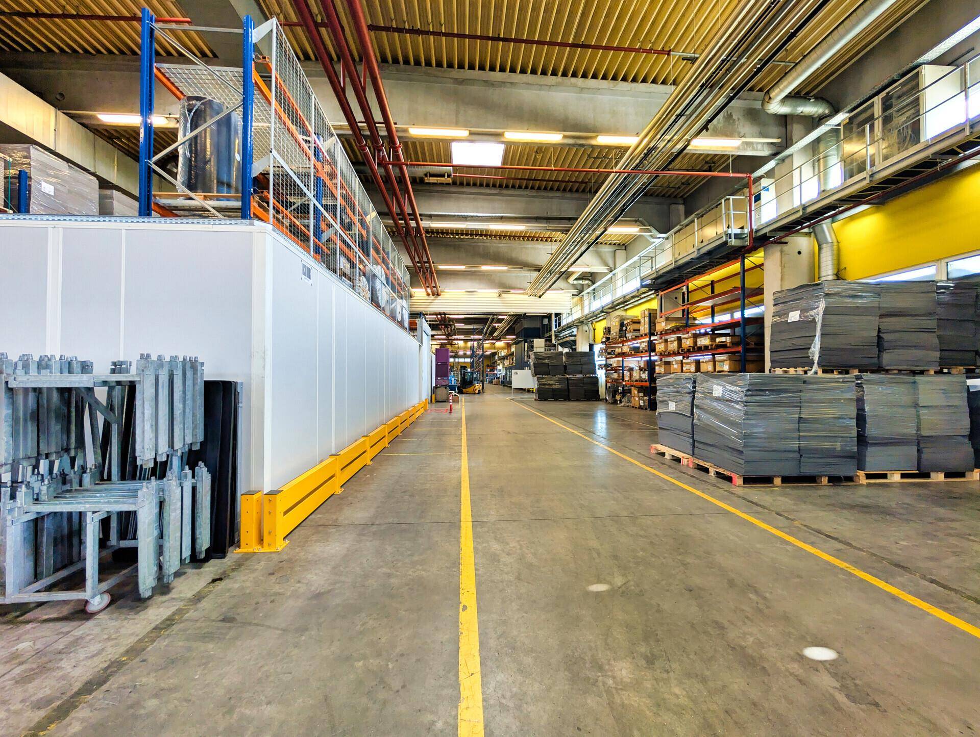 Innenansicht einer Lager- oder Produktionshalle mit hohen Decken, Industrieregalen und gestapelten Materialien auf Betonboden.