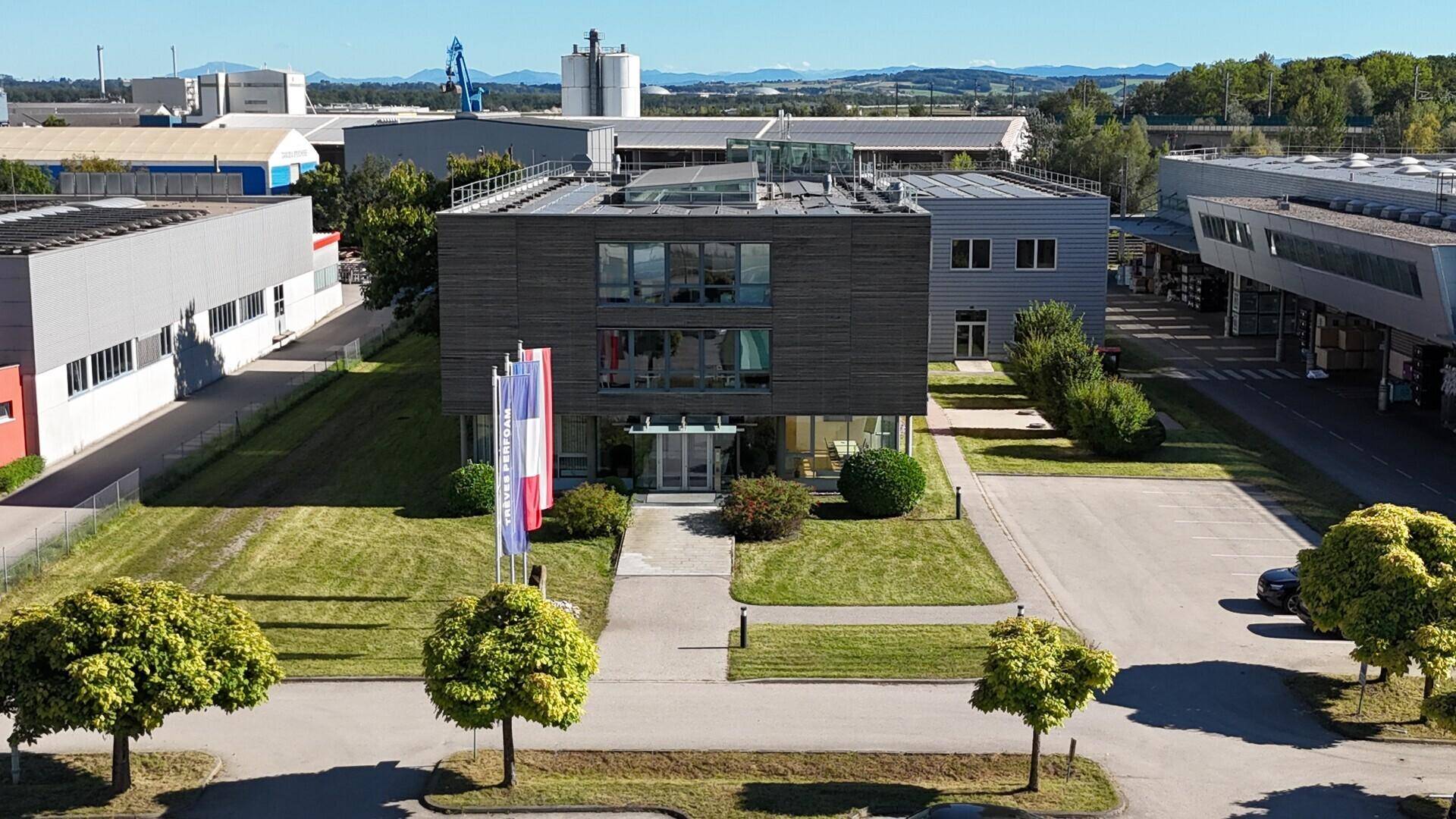 Modernes Bürogebäude mit dunkler Fassade, großen Fenstern, gepflegtem Rasen und einer Auffahrt mit Fahnen.